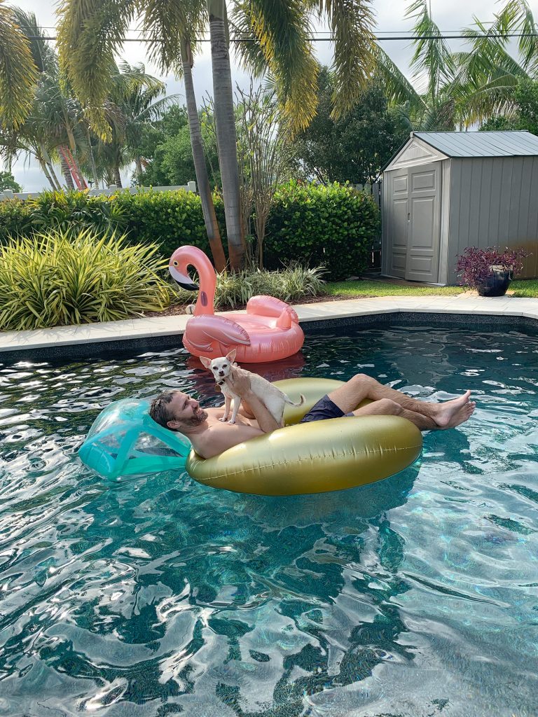 John in pool float with Burger on chest with flamingo float in background