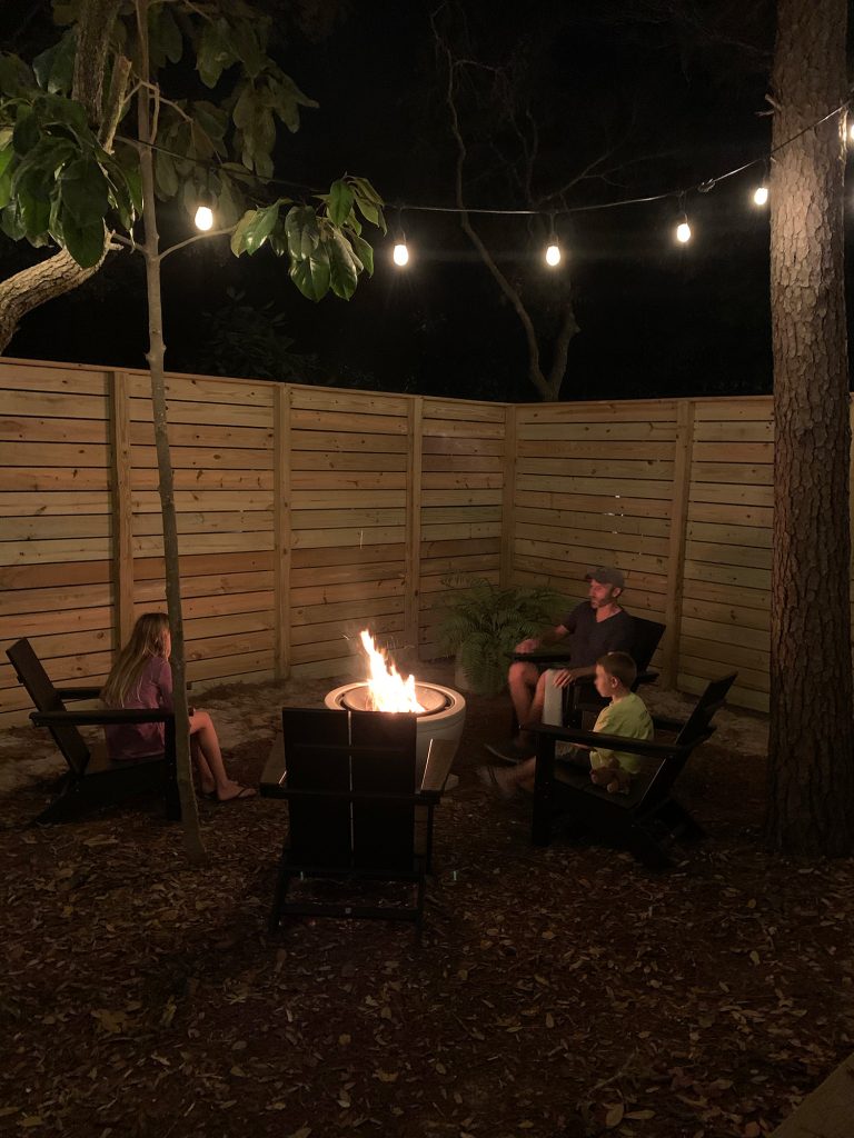 Family sitting around fire pit with unpainted fence