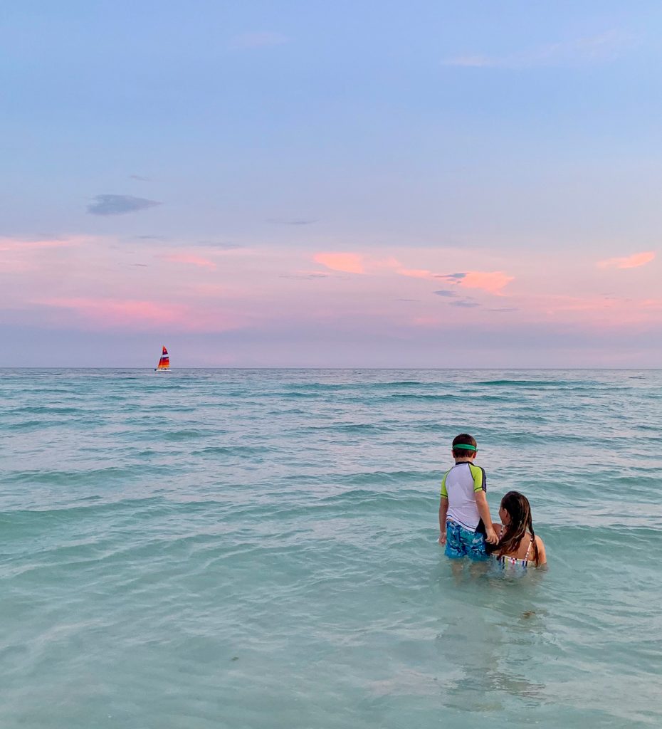 Kids playing in Gulf of Mexico at sunset with sailboat in background