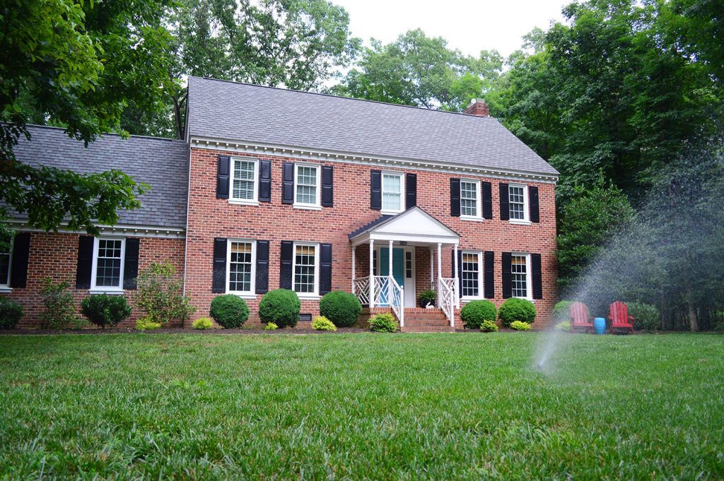 Brick House With Irrigation Sprinkler System Running In Front Yard