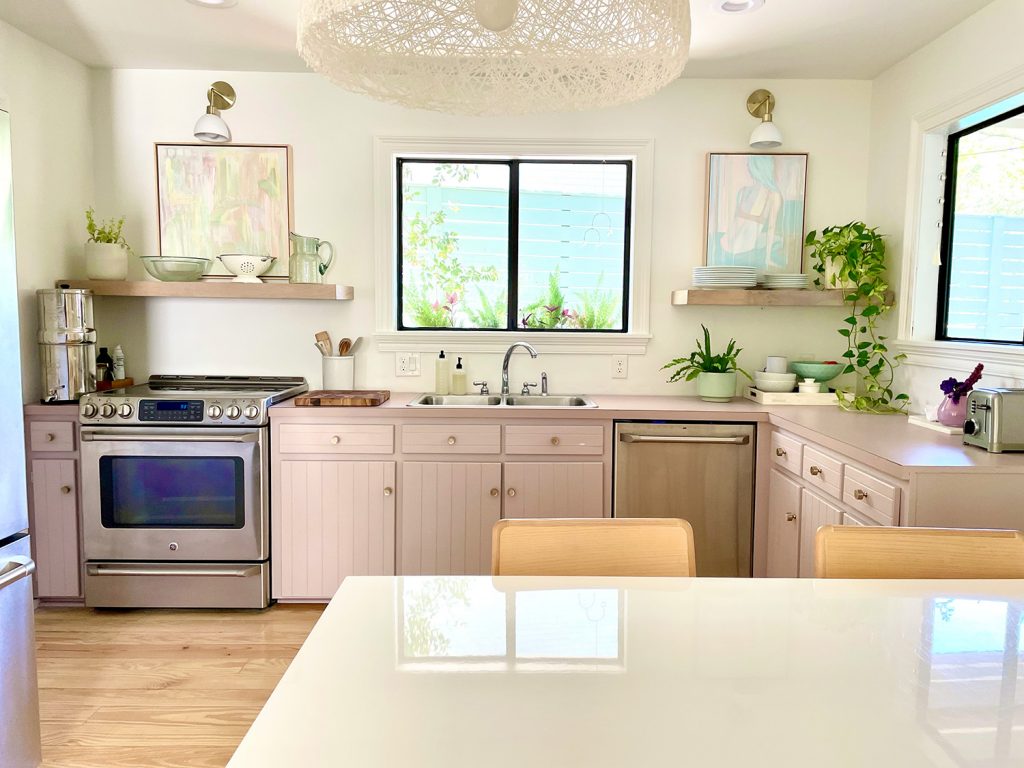 Straight View Of Beach Kitchen With Pink Mauve Cabinets And Floating Shelves
