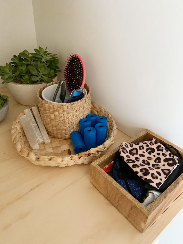 Baskets and bins on laundry shelf holding entryway accessories like masks dog bags and sunglasses