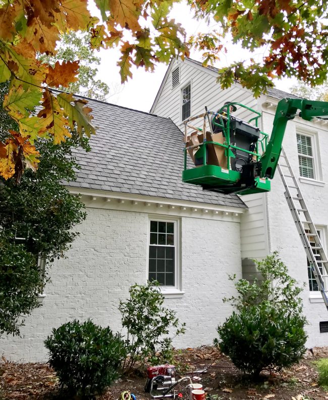painter in crane painting siding of a brick house white