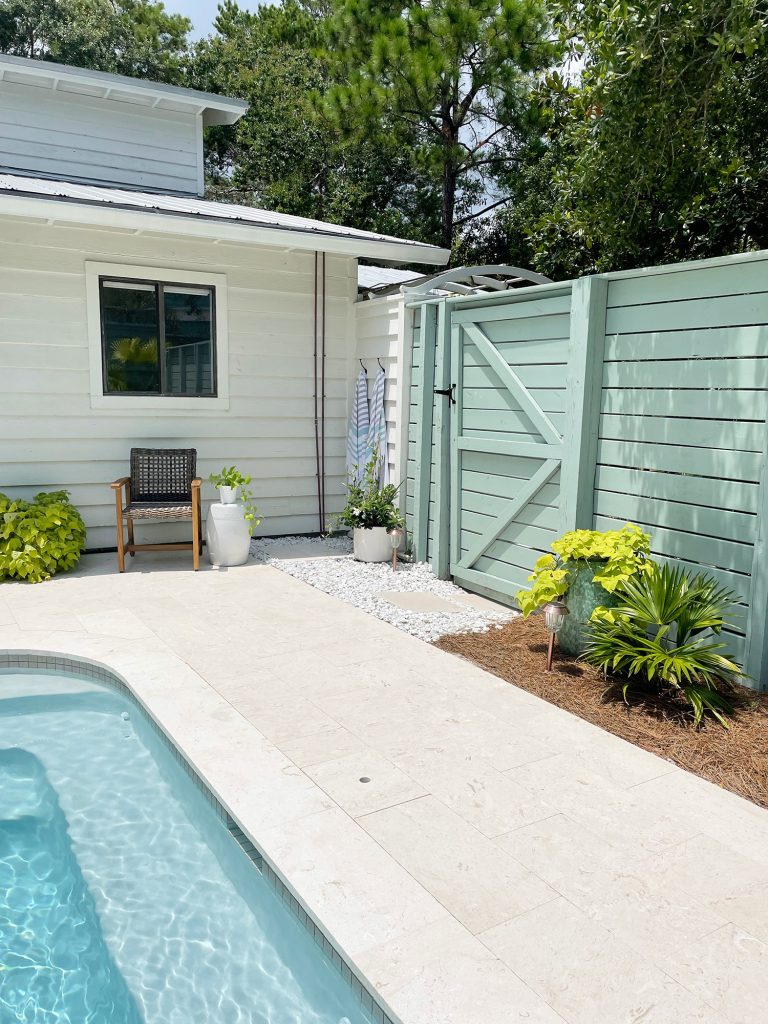 Horizontal slat gray green wood fence around pool area with gate near house
