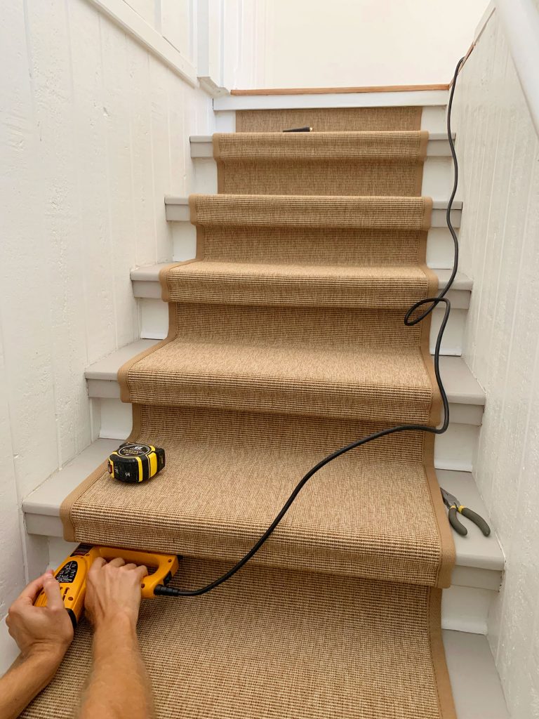 Hand Pushing Electric Stapler Into Underside Of Stair Tread To Secure Sisal Runner